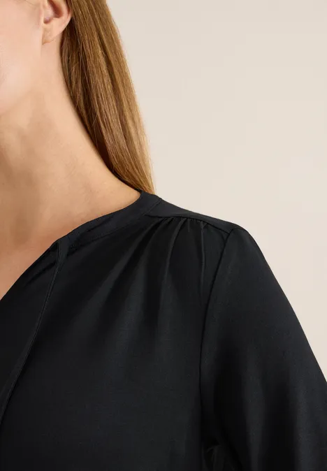 Nahaufnahme einer Frau mit langen blonden Haaren in einer schlichten schwarzen Bluse.